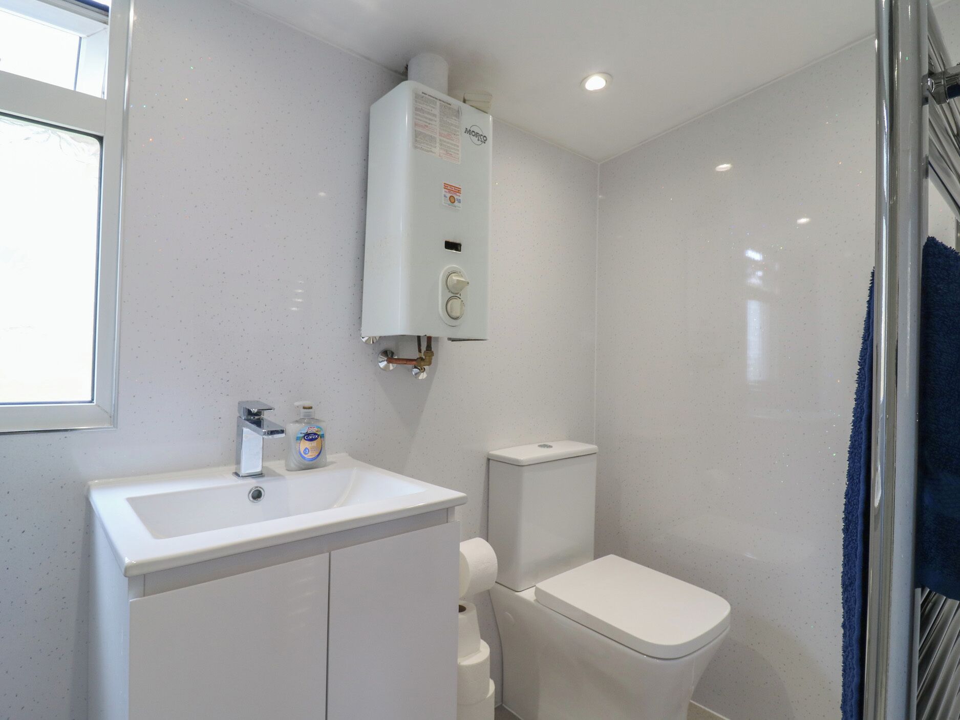 Un baño con un lavamanos blanco, inodoro y calentador de agua instalado en la pared.