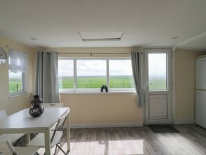 Una habitación con un gran ventanal, una mesa con sillas, un florero y una puerta que da a otra estancia.