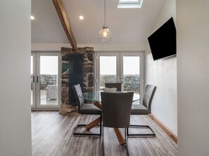 Ein Essbereich mit einem Glastisch, Stühlen, einer Wand aus Stein und Blick durch große Fenster.