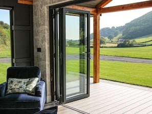 Una habitación con puerta de vidrio corredera que da a una terraza, un sillón mullido y vistas a un paisaje verde.