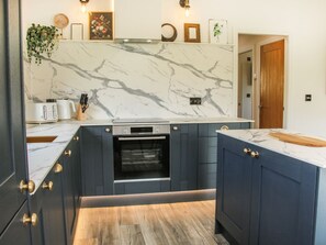 A kitchen with a marble backsplash, dark cabinetry, and a built-in oven. - Meadow View, Meifod, Powys (Meifod)