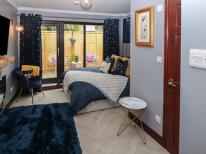Ein Schlafzimmer mit einem Bett, einem kleinen runden Tisch, einem Sessel, einem Fernseher und einer Tür.