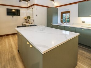 A modern kitchen with a large island, wooden flooring, and green cabinets. - Winding Wheel Cottage, Cambois (Blyth)