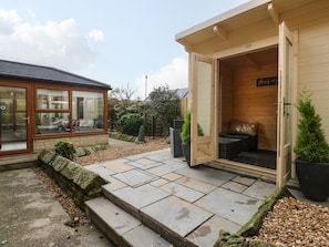A wooden building with a glass door open, a stone pathway, and a small garden with plants. - Winding Wheel Cottage, Cambois (Blyth)