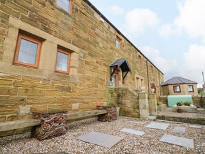 A stone building with a bench, a small garden area, and a pathway leading to a door. - Winding Wheel Cottage, Cambois (Blyth)