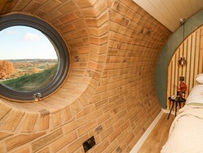 A room with a brick wall, a circular window, a bed, and a small table with a lamp. - Tan y Wawr- Onnen, Llanfair Caereinion (Welshpool)