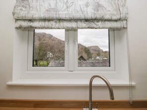 A window with a white frame, a metal faucet, and a patterned valance.