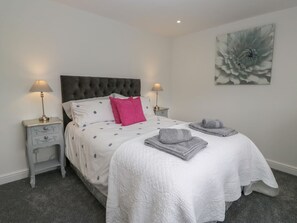 A bedroom with a bed, two bedside tables, a wall art piece, and a carpeted floor.
