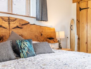 A bedroom with a large wooden headboard, a bed with floral bedding, a nightstand with a lamp, and a wooden door. - The Lodge, Chester: Cozy Retreat (Chester)