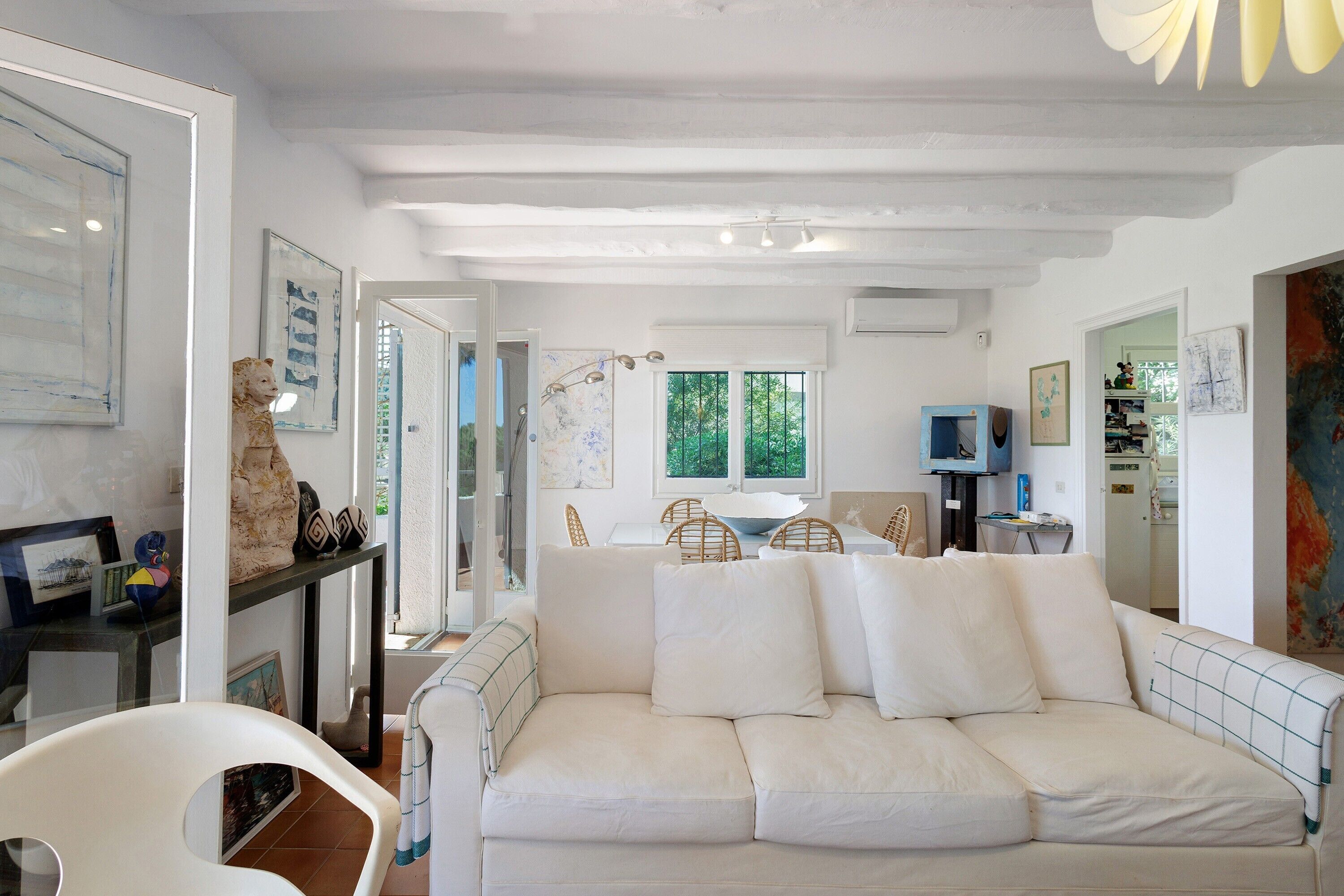 A modern living room with a white sofa, a dining area with wicker chairs, and artwork on the walls.
