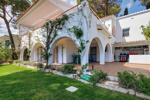 A white building with arches, a covered patio, and a small garden.