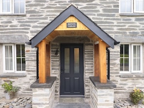 A stone building with a black door, a wooden porch, and a sign reading 'BWTHYN CAMLAN'. - Bwthyn Camlan, Dinas Mawddwy (Machynlleth)