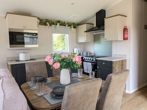 Una cocina moderna con comedor, que incluye estufa, microondas y un florero con flores sobre la mesa.