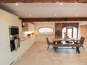A kitchen with white cabinets, a built-in oven, and a dining area with a wooden table and chairs. - The Mill House, Thirsk (Thirsk)