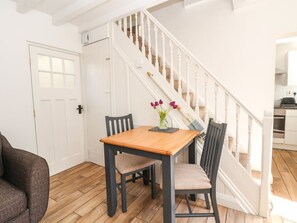 A dining area with a wooden table and chairs, a staircase, and a white door. - Sandy Shell Cottage, Conwy (Conwy)