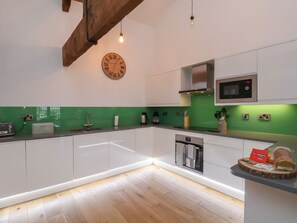 A modern kitchen with white cabinets, a green backsplash, a wooden ceiling beam, a clock, and a built-in oven. - Repton @ Engine Shed - Whitby Retreat (Whitby)
