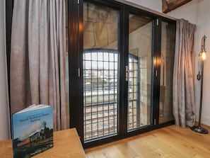 A room with a large sliding glass door leading to a view of railway tracks, a book titled 'An Historical History of the North Yorkshire Moors Railway' on a table, and a floor lamp. - Repton @ Engine Shed - Whitby Retreat (Whitby)