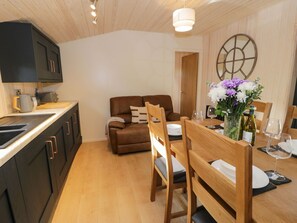 A modern kitchen with dark cabinets and a wooden dining table set for two. - Math (Lodge 3), in Llanelidan. (Ruthin)