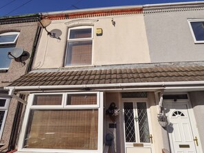 Ein zweistöckiges Haus mit einem Ziegeldach, einer Haustür mit Fensterteil und einer Satellitenschüssel an der Seite.