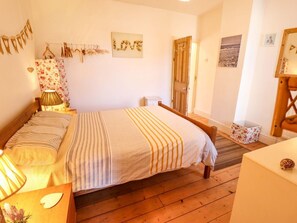 Ein Schlafzimmer mit einem Bett, Holzboden, einem Nachttisch mit Lampe, einer Kommode und einer Tür.