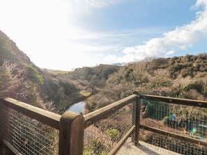 Blick von einer Brücke über ein Tal mit einem Fluss, umgeben von Hügeln und Vegetation.
