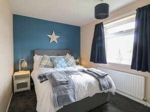 Ein Schlafzimmer mit Bett, Nachttisch, Lampe, einer Stern-Dekoration und einem Fenster mit Vorhängen.