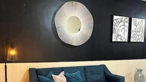En moderne stue med en mørkeblå sofa, et rundt spejl og to billeder i rammer på væggen.