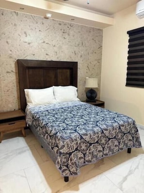 A bedroom with a bed, a nightstand, a lamp, and a window with blinds. - Standard 2-bedroom apartment, Suite 4 Anchor Suites (Puerto Peñasco)