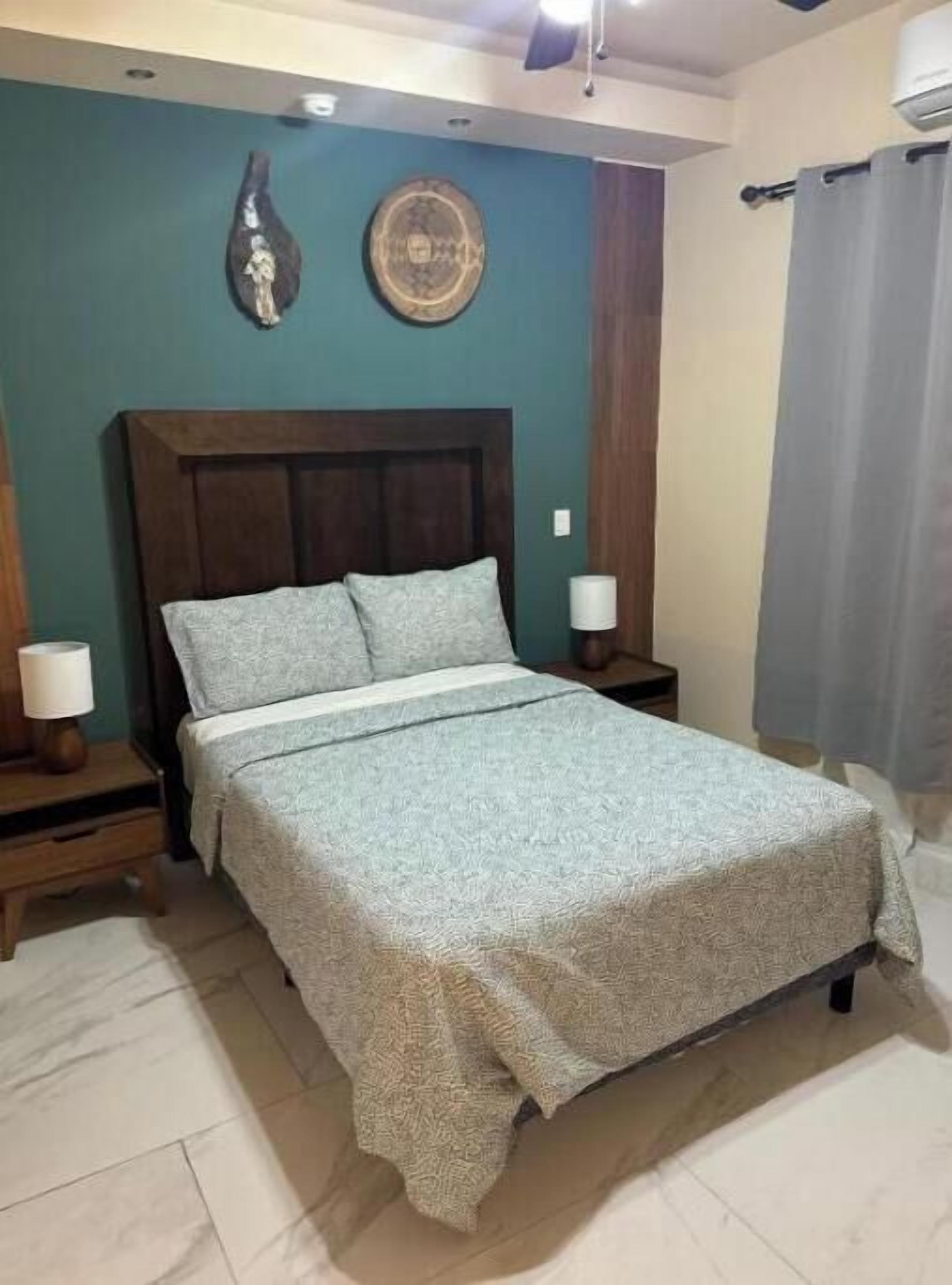 A bedroom with a bed, two bedside tables, a wall clock, and a curtain.