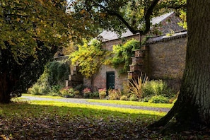 A brick building with a green door, surrounded by a garden with various plants and a tree. - Lytham Hall Gate House, Lytham St. Annes (Lytham St. Annes)