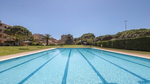 Une piscine aux eaux cristallines, avec des lignes de démarcation bleues, entourée de pelouse et d’arbres bien entretenus, et des bâtiments en arrière-plan.