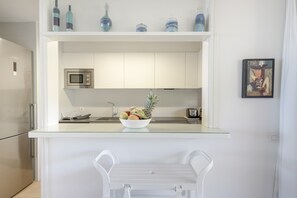 A modern kitchen with a glass-top island, white cabinetry, a microwave, and a bowl of fruit.