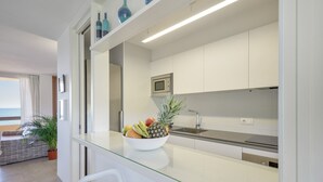 Une cuisine moderne avec un plan de travail en verre, un saladier rempli de fruits, un four à micro-ondes et une vue sur l’océan.