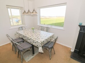 A dining area with a table, chairs, a window, and a fireplace. - Happy Daze, Morfa Nefyn (Pwllheli)