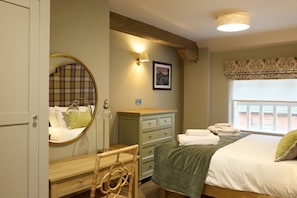 Ein Schlafzimmer mit Bett, Schminktisch, Spiegel, Lampe und Fenster mit Blick.
