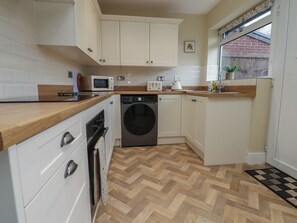 A compact kitchen with white cabinets, a microwave, a toaster, a washing machine, and a wooden countertop.