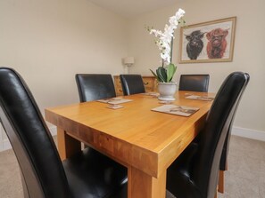 A dining table with chairs, a vase with flowers, and a framed picture on the wall.