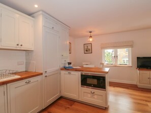 A kitchen with white cabinets, a wooden countertop, a built-in oven, and a window with a view. - Greenham Rise, Norton-Sub-Hamdon (Stoke-Sub-Hamdon)