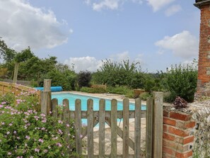 A swimming pool surrounded by a wooden fence, with a brick wall and greenery in the background. - Byre Cottage 2 (2 bed), Storrington (Pulborough)