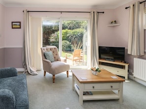 A living room with a sofa, a chair, a coffee table, a TV, and a sliding glass door leading to a garden. - Altair, Freshwater, Isle of Wight (Freshwater)