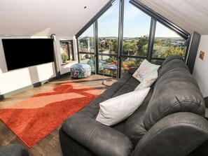 A modern living room with a large sofa, a flat-screen TV, and a view through large windows. - 11 Brython Place, Tenby (Tenby)