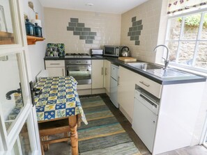 A compact kitchen with a stove, microwave, sink, and cabinets. - Sally's Cottage, Carleton-In-Craven (Skipton)