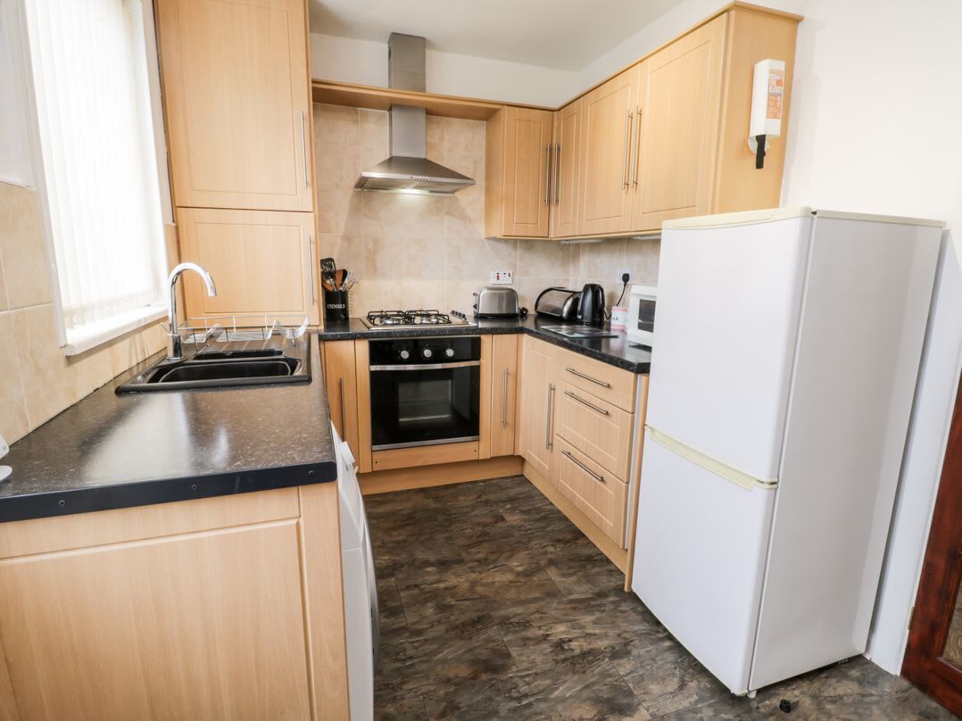 A compact kitchen with wooden cabinets, a gas stove, an oven, a microwave, and a white refrigerator.