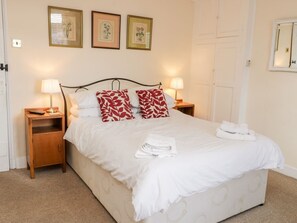 A neatly made bed with white bedding and red patterned pillows, two bedside lamps, and framed botanical prints on the wall.
