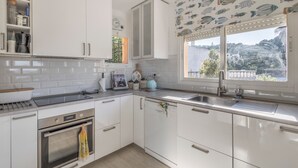 Une cuisine avec des meubles blancs, un four en acier inoxydable, un évier et une fenêtre donnant sur une colline.