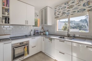 A kitchen with white cabinets, a stainless steel oven, a sink, and a window with a view of a hillside.
