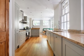 A kitchen with wooden flooring, white cabinets, a central island, and large windows. - 32 Park Street, Windsor, Berkshire (Windsor)