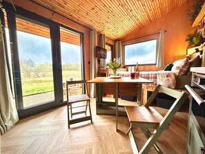 Ein Zimmer mit Holzboden, großen Fenstern, einem Esstisch, Stühlen, einer Couch und einem Fernseher.