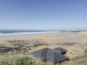 A beach with rocky terrain, a clear sky, and a distant building. - 38 Surf View, Newquay (Newquay)