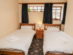 Ein Zimmer mit zwei Einzelbetten, einem kleinen Nachttisch mit Lampe, einem gemusterten Teppich und einem Fenster mit Vorhängen.